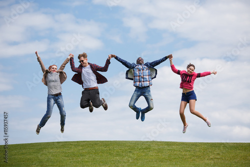 Happy best friends holding hands and jumping in air all together while posing for photographer on picnic in park.
