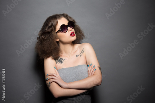 Portrait of beautiful model lady in sunglasses looking upwards while posing in studio. Pretty woman with modern hairstyle posing with her arms crossed or folded.