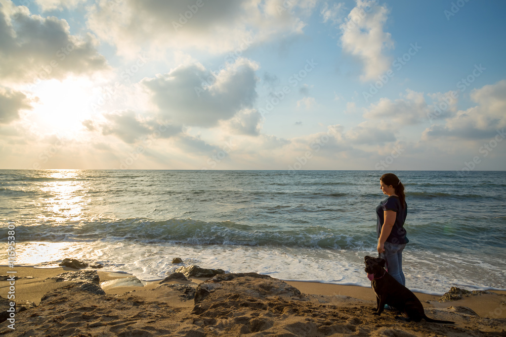 woman looks at the sunset with a dog