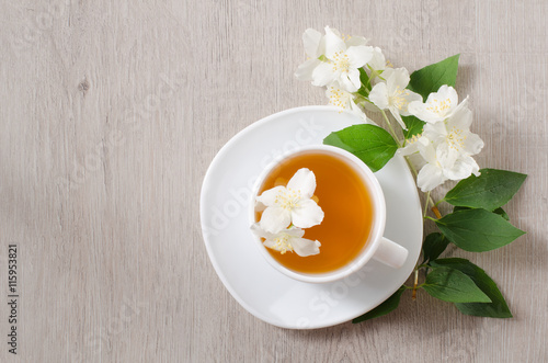 Top view of a mug of herbal tea and jasmine flowers on a wooden table, space for text