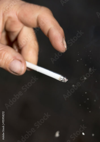 Fototapeta Naklejka Na Ścianę i Meble -  smoking a cigarette in his hand on black