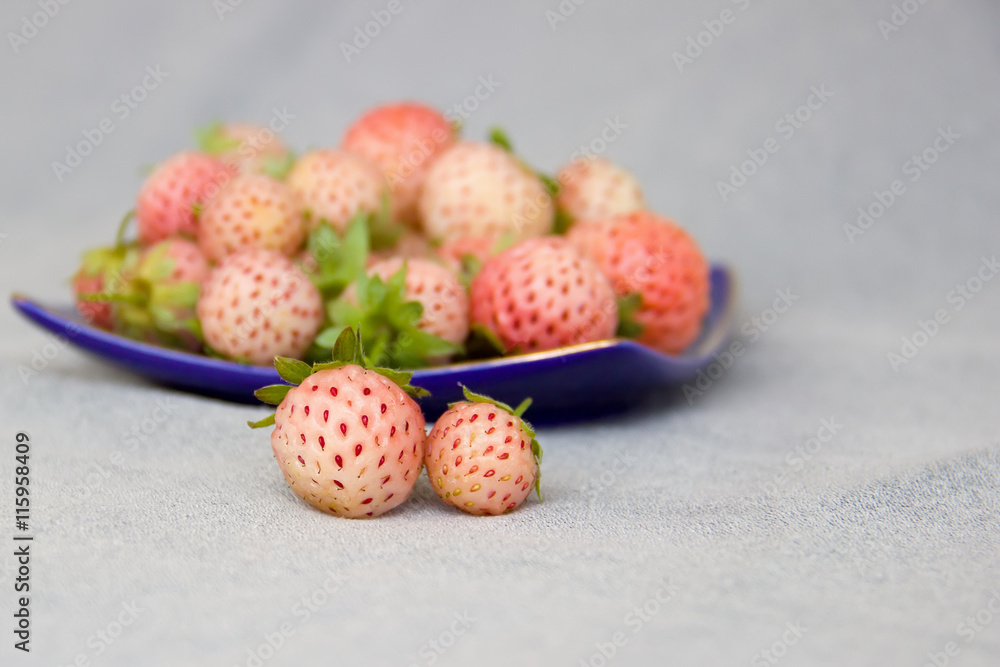 Two pineberries in front of a saucer with pineberries