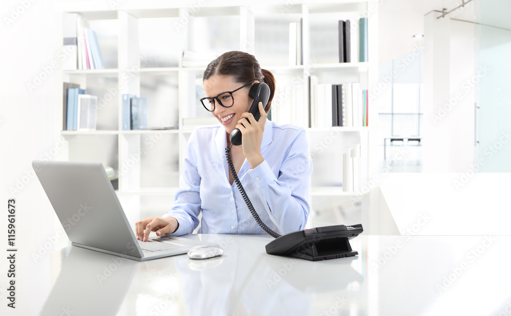 smiling woman in office at desk with computer, talking on the ph smiling woman in office at desk with computer, talking on the ph