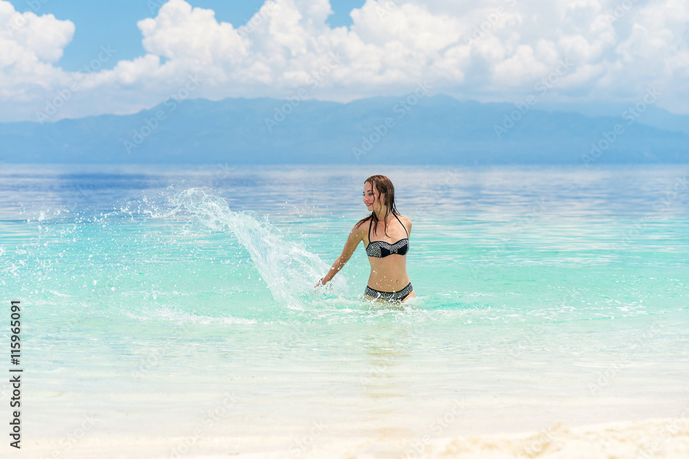 Young european woman in bikini with good mood splashing and dancing in beautiful tropical calm sea under cloudy soft sky