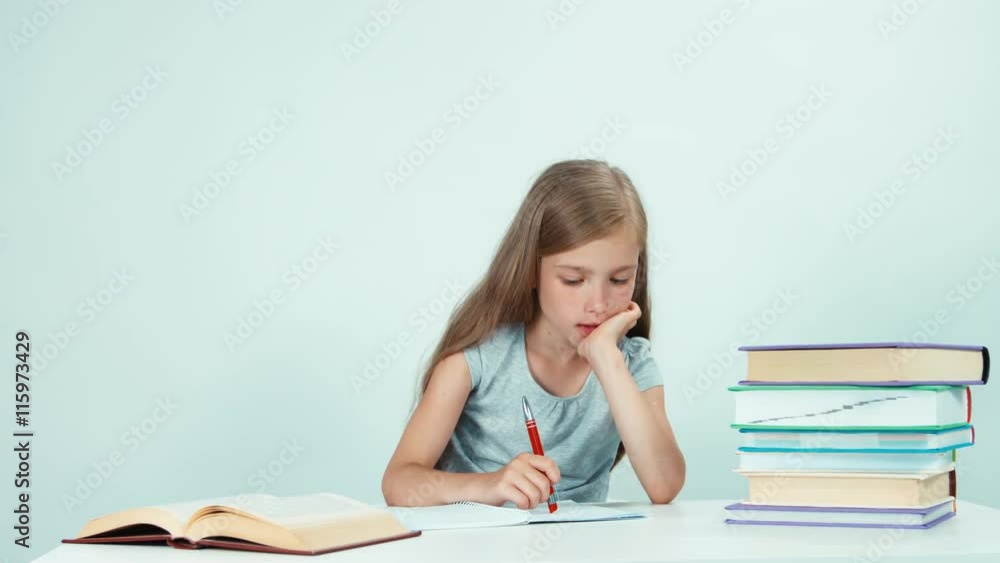 Schoolgirl writing in her notebook. Child girl sitting at the table on white background Schoolgirl writing in her notebook. Child girl sitting at the table on white background