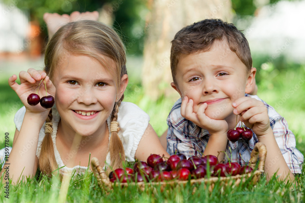 Happy little children lying near the tree with a basket of cherr Happy little children lying near the tree with a basket of cherr