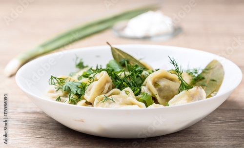 plate of traditional Russian dumplings sprinkled with herbs on wooden table