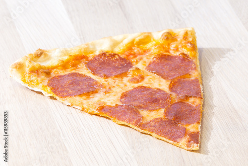 Slice of the italian classic pepperoni pizza on a wooden chopping board
