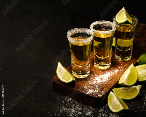 Fototapeta Mexican Gold Tequila with lime and salt on wooden table, selective focus