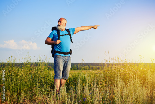 Active aged man with rucksack pointing at something in the field © ArtFamily