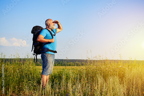 Physically fit aged man with rucksack looking at sunlight