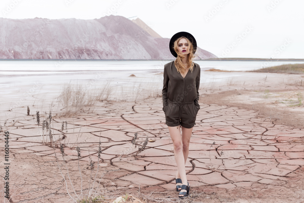 Fototapeta premium fashion shot of a beautiful sexy girl in a black hat is removed in the desert for the magazine