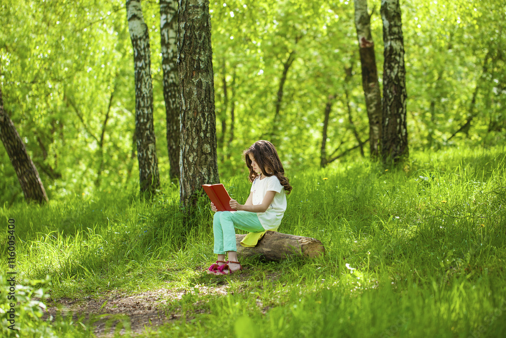 Charming little girl in forest with book sitting on tree stump Charming little girl in forest with book sitting on tree stump