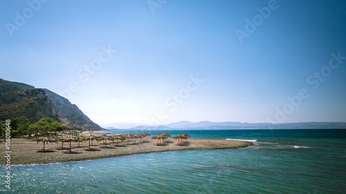 Straw umbrella on a sandy beach in Greece. Beach chairs with umbrellas on a beautiful beach in Crete island.