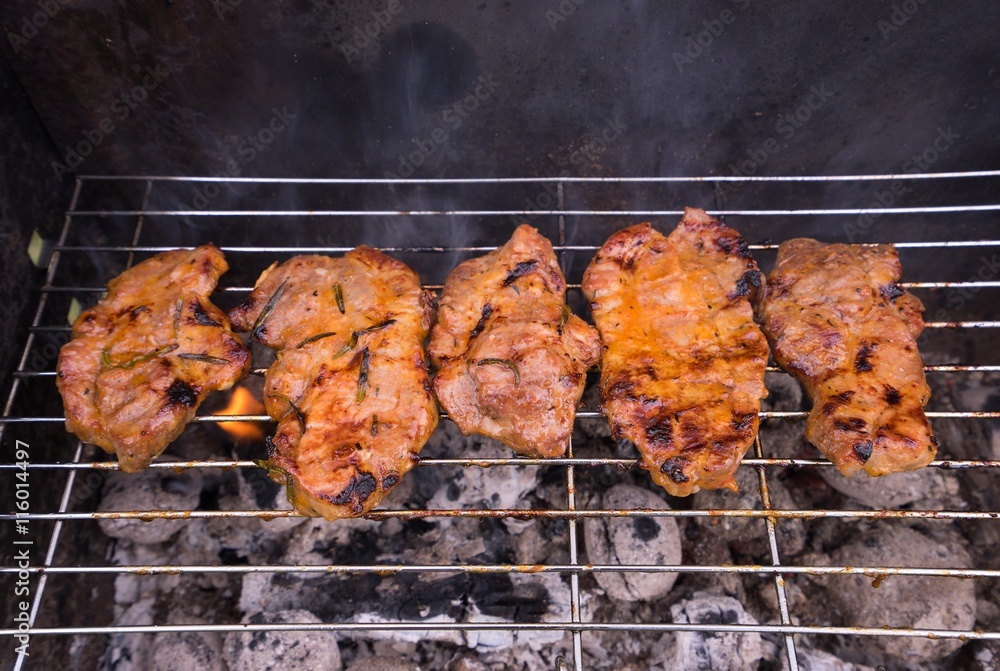 Marinated pork steaks on the grill. Steaks marinated in the olive oil and honey with the curry and chili spice and herbs like rosemary and thyme. Party food for home garden summer parties.