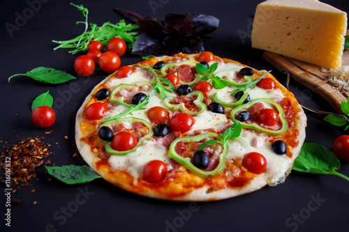 Homemade pizza with salami, black olives and basil.