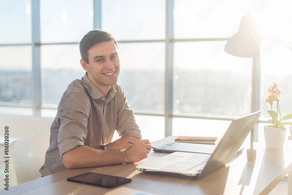 Man using laptop on his workplace. sitting, smiling, looking at camera. Man using laptop on his workplace. sitting, smiling, looking at camera.