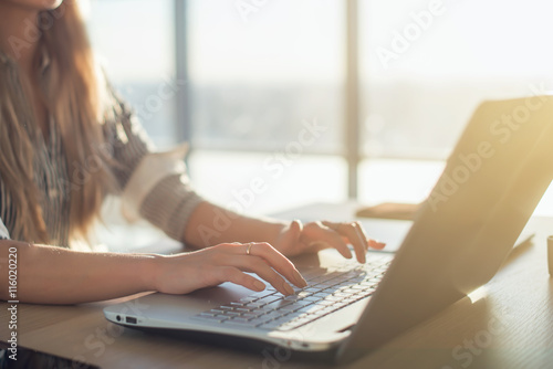 Female writer typing using laptop keyboard at her workplace in the morning. Woman writing blogs online, side view close-up picture.