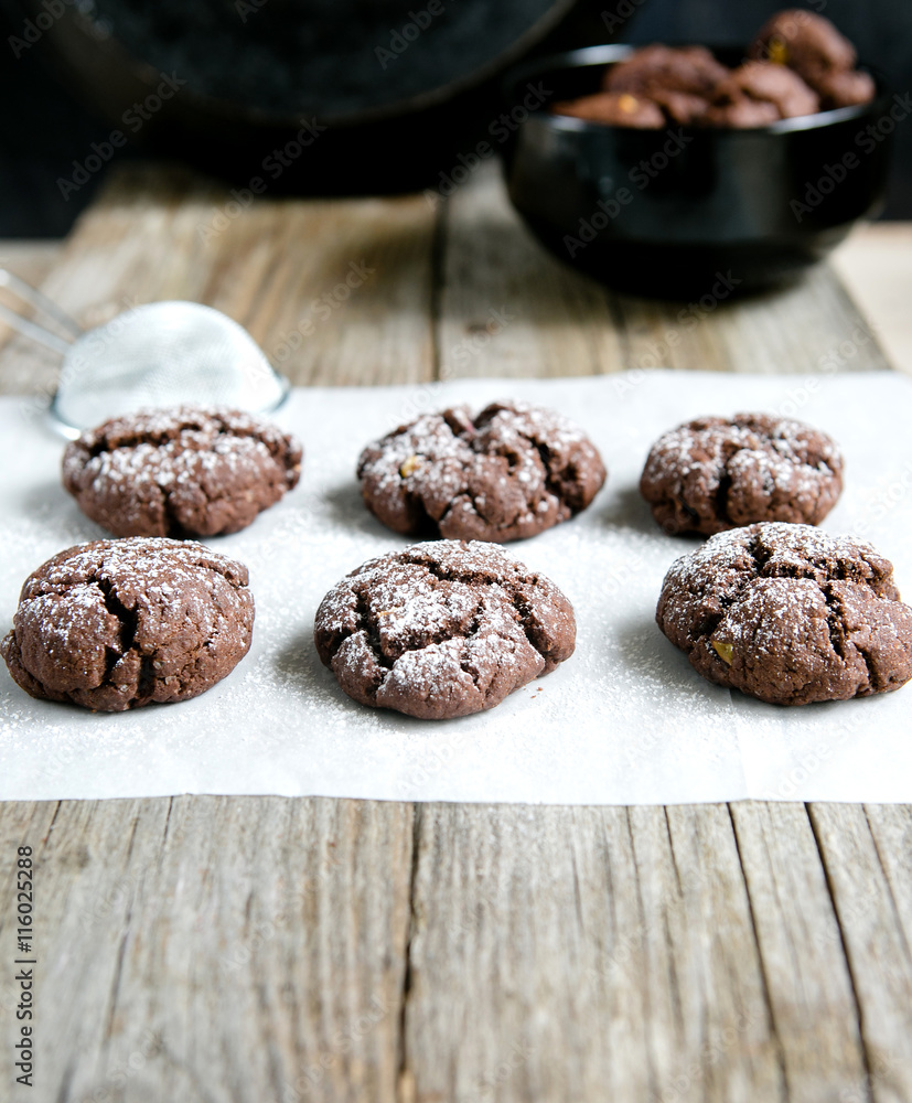 Chocolate cookies on kraft paper, sprinkled with powdered sugar on a wooden background Chocolate cookies on kraft paper, sprinkled with powdered sugar on a wooden background