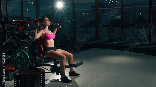 Young woman pumping muscles on gym machine photo