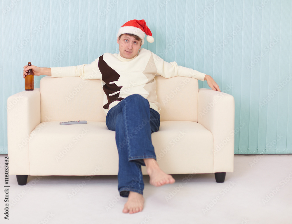 Man in a New Year's cap sits on sofa with bottle
