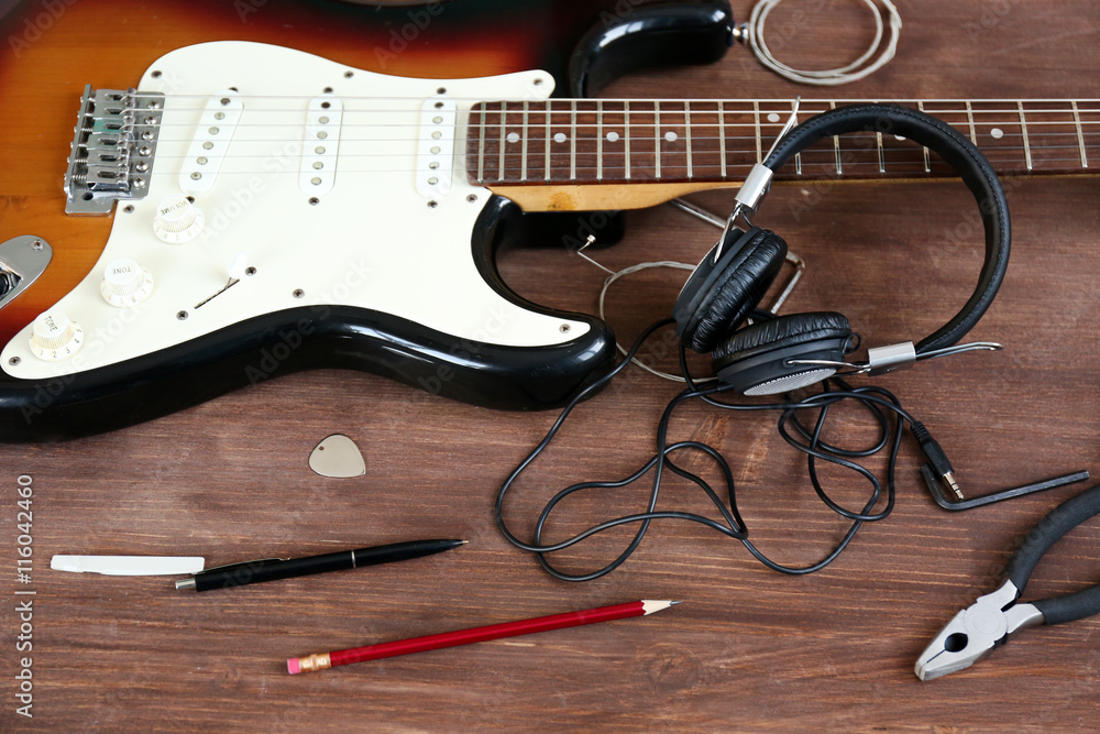 Naklejka premium Guitar with headphones on wooden surface closeup