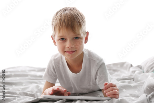 Cute little boy playing with tablet on bed photo