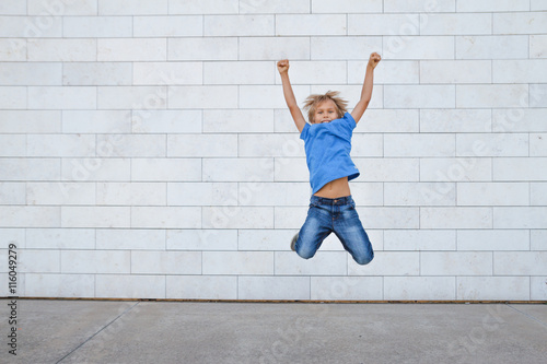 Happy little boy jumping. Urban gray background. People, childhood, happiness, freedom, movement concept