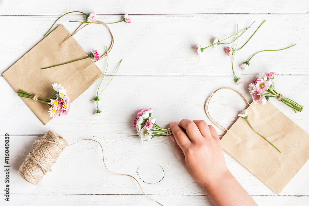Workspace with small bouquets of daisy flowers, paper bags. Creation. Child's hand. Top view, flat lay Workspace with small bouquets of daisy flowers, paper bags. Creation. Child's hand. Top view, flat lay