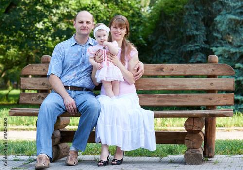 happy family portrait on outdoor, group of tree people sit on wooden bench in city park, summer season, child and parent