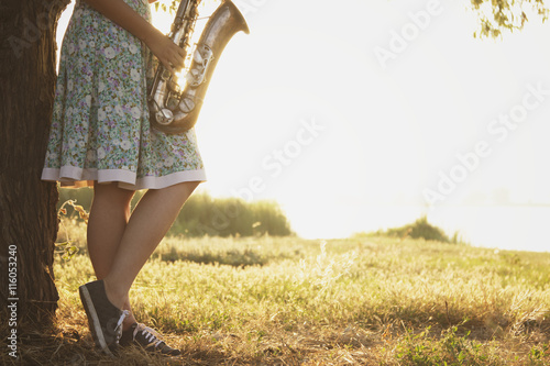 young woman in a dress stands near the tree on the green grass with a wind musical instrument in the hands of dawn
