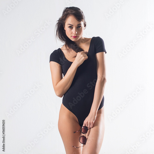 Cute brunette female model posing, wearing black one piece underwear suit, touching her hair ends, on white background, not isolated. © undrey