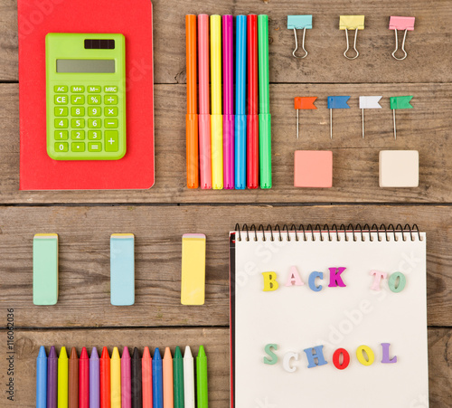 inscription of "back to school", calculator, notepads, markers and other stationery on brown wooden table