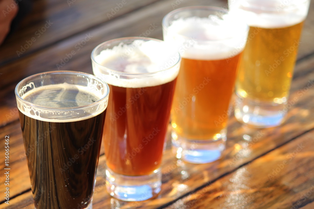 A selection of four craft beers during a tasting session on a wooden table - obrazy, fototapety, plakaty 