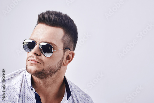 closeup portrait of a casual young man with sunglasses looking at the camera. on gray background