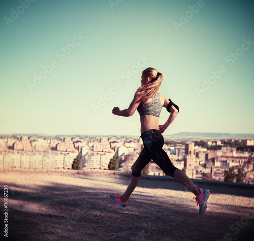 Portrait of woman runner in motion. Young energetic girl training in the countryside summer day. 