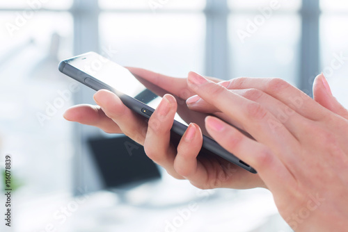 Close-up side view picture of female hands holding smartphone, using apps and wi-fi internet, reading messages.