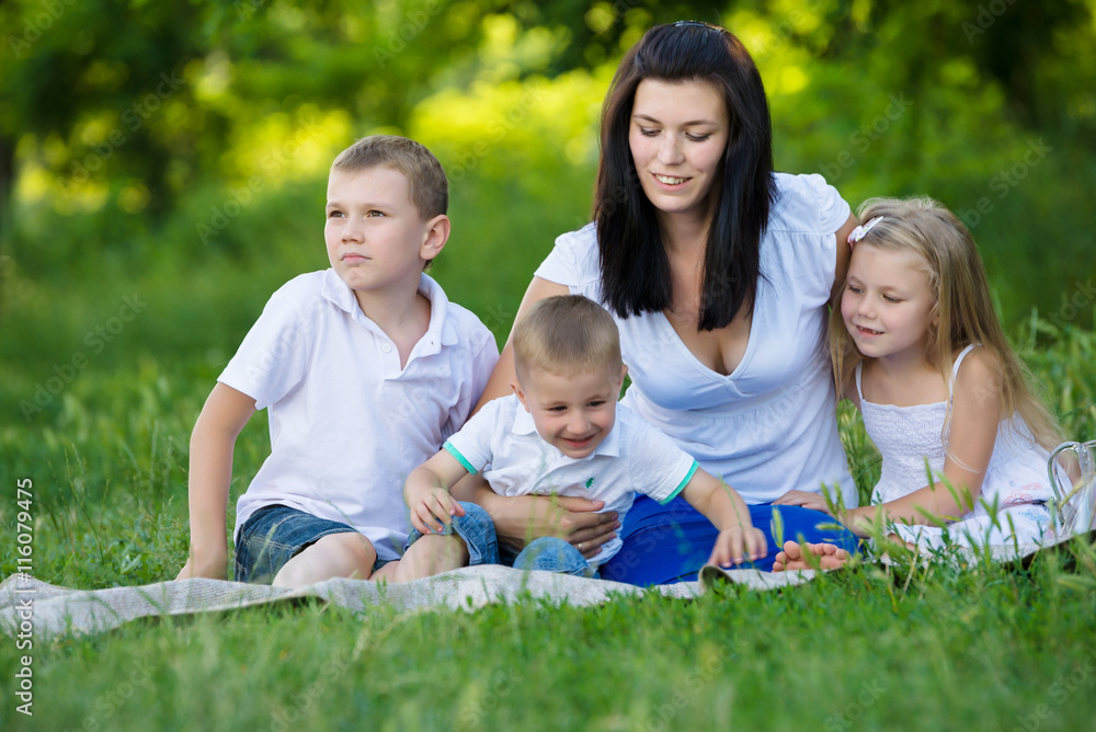 Happy mother, two sons and daughter dressed in white shirts are sitting on the grass in the park Happy mother, two sons and daughter dressed in white shirts are sitting on the grass in the park