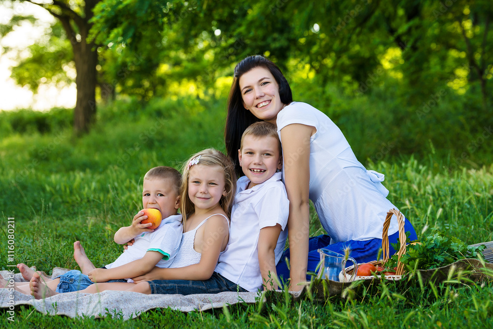 Happy mother, two sons and daughter dressed in white shirts are sitting on the grass in the park Happy mother, two sons and daughter dressed in white shirts are sitting on the grass in the park