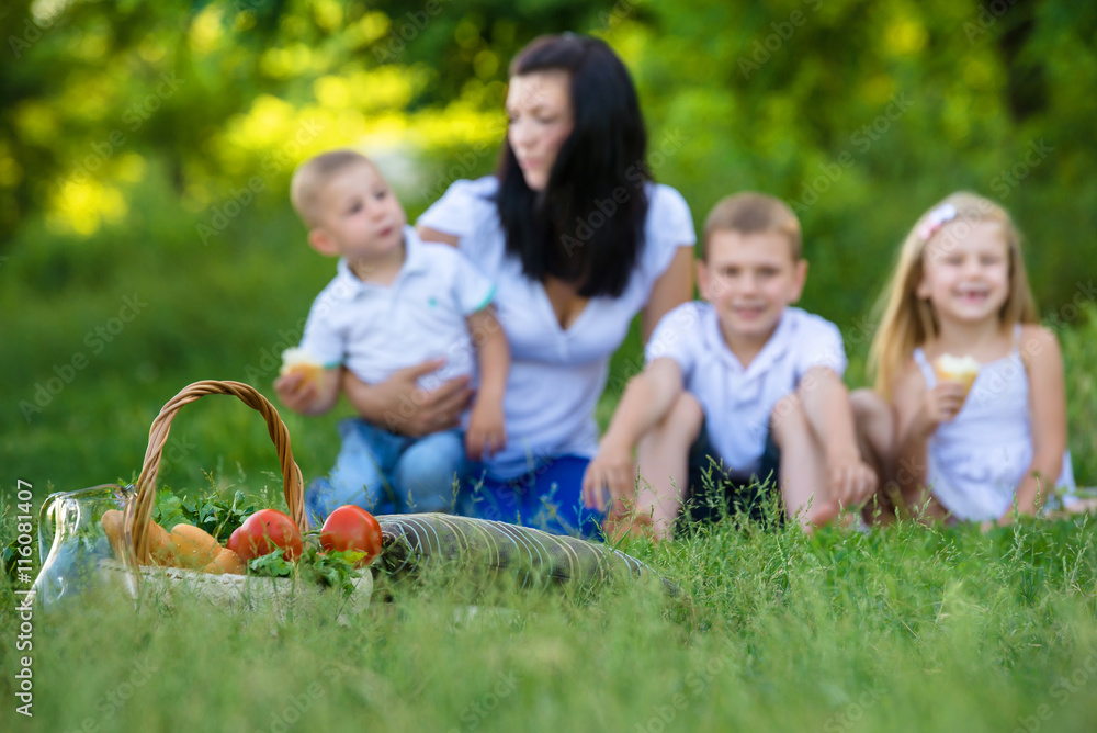 Happy mother, two sons and daughter dressed in white shirts are sitting on the grass in the park Happy mother, two sons and daughter dressed in white shirts are sitting on the grass in the park