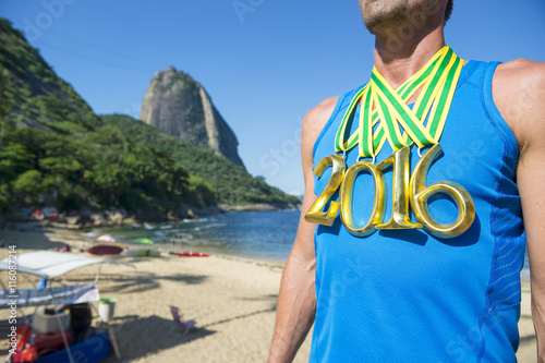 First place 2016 athlete wearing gold medals standing on the beach in front of Sugarloaf Mountain in Rio de Janeiro, Brazil