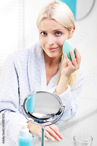 Gąbka do nakładania makijażu. Kobieta nakłada podkład na skórę twarzy za pomocą specjalnej gąbki makijażu.