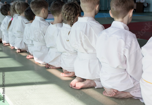 Tableau sur toile Group of children in kimono sitting on tatami on martial arts training seminar