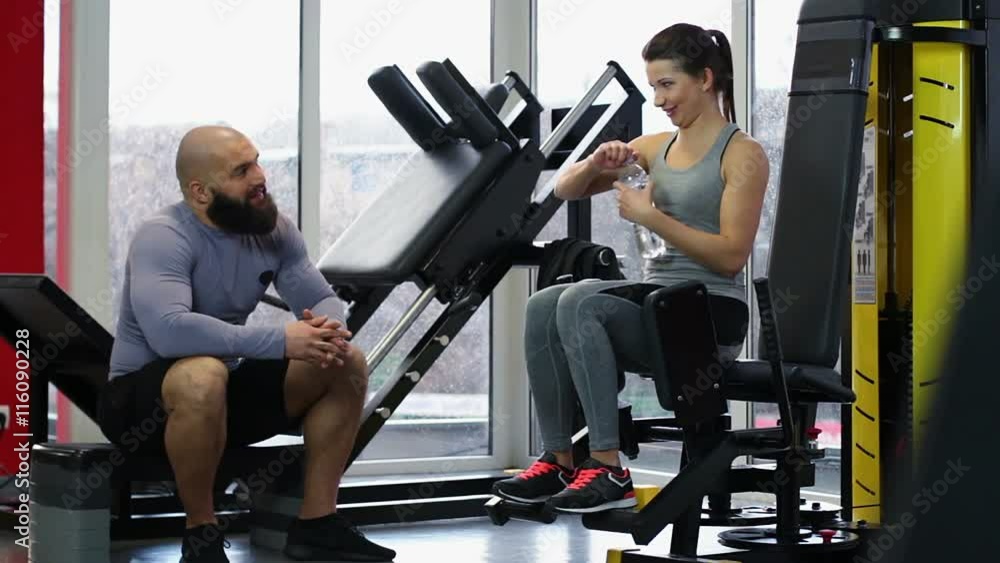 Man giving bottle of fresh drinking water to woman during active workout in gym Man giving bottle of fresh drinking water to woman during active workout in gym