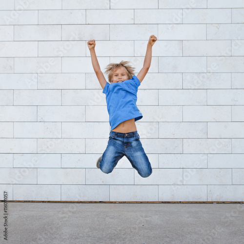 Happy little boy jumping over gray urban background. People, childhood, happiness, freedom, movement concept