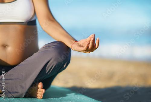 Pregnant woman doing yoga on the beach. Soft light. Beautiful girl with a swimsuit. Sea. She relax yoga. Young healthy woman practicing yoga on the beach at sunset 