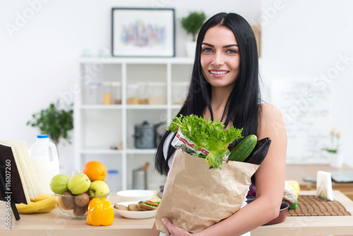 Close-up portrait of a woman holding paper bag full fresh vegetables. Happy smiling female vegetarian with grocery.