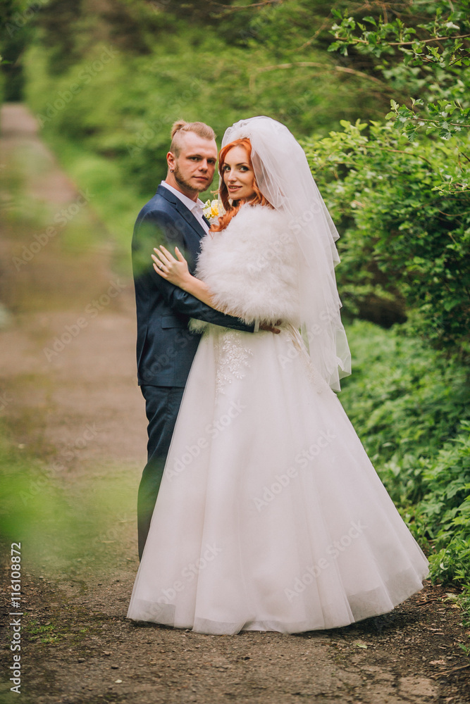 bride and groom holding hands in a stylish outfit on a background of the forest road. bride and groom holding hands in a stylish outfit on a background of the forest road.