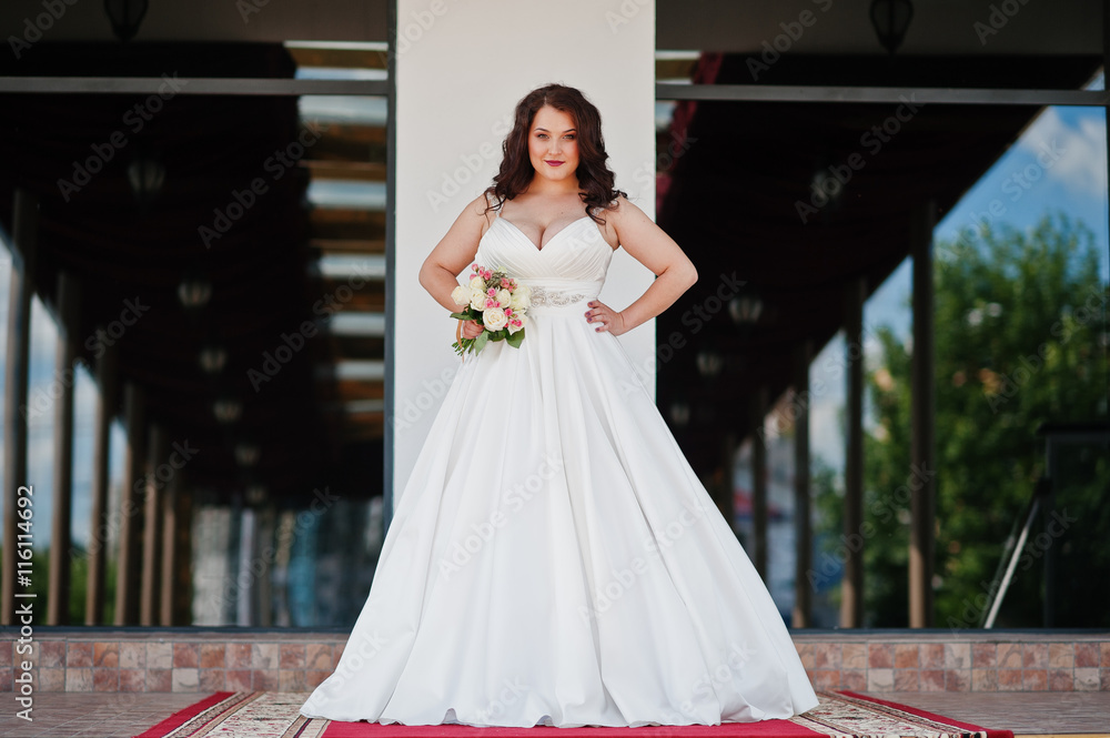 Naklejka premium Big breasts brunette bride with wedding bouquet posed at wedding