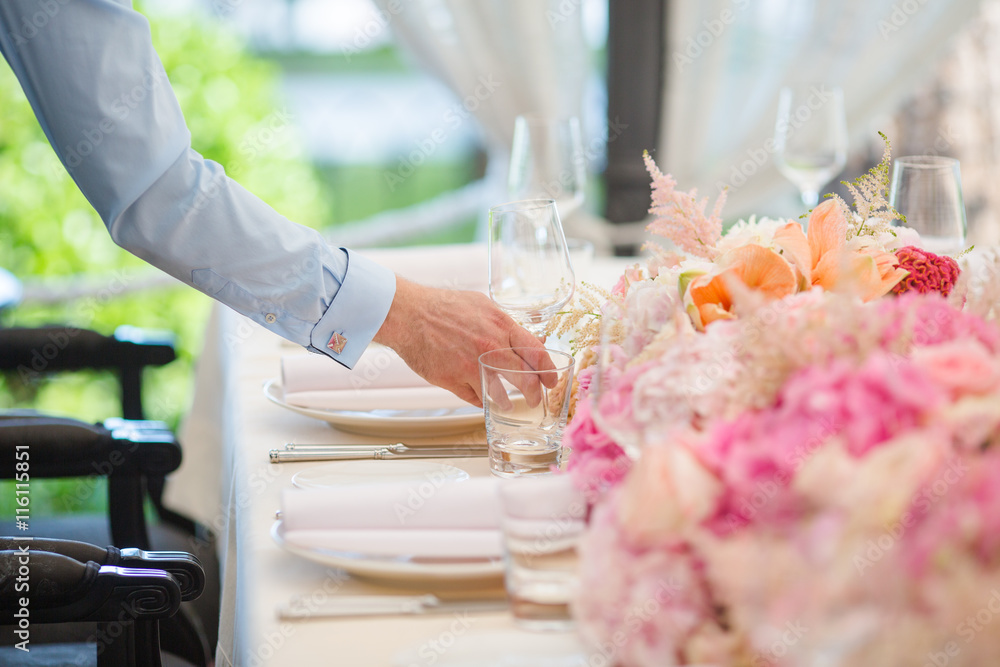 Waiters is serving dinner place on a wedding in a restaurant. Table decorated with flowers Waiters is serving dinner place on a wedding in a restaurant. Table decorated with flowers